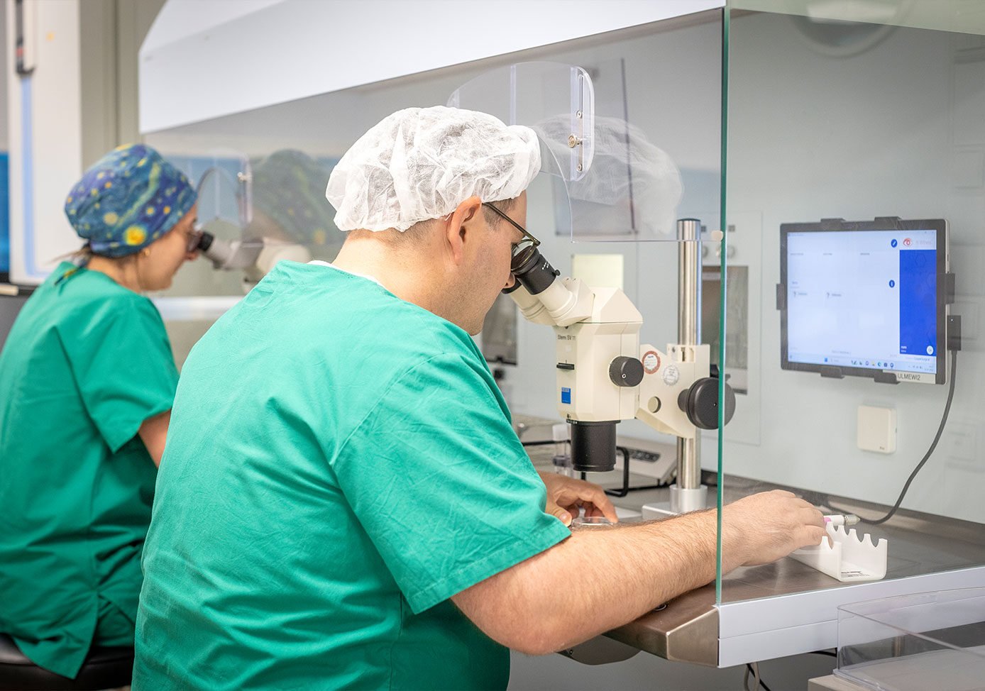 Zwei Labormitarbeiter von Next Fertility Ulm blicken durch zwei Mikroskope.